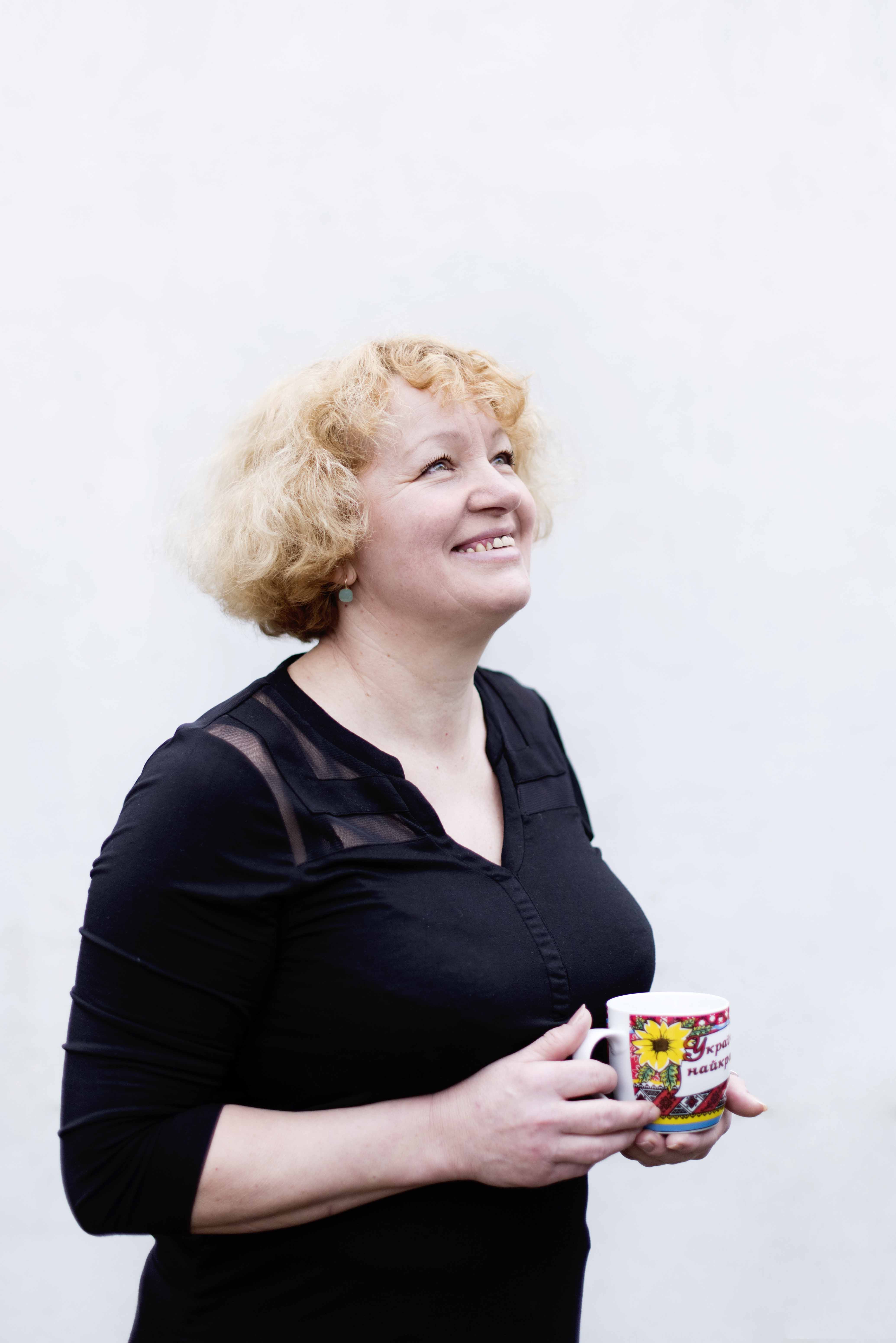 Anna looks upwards smiling towards the sky, holding her Ukrainian mug.