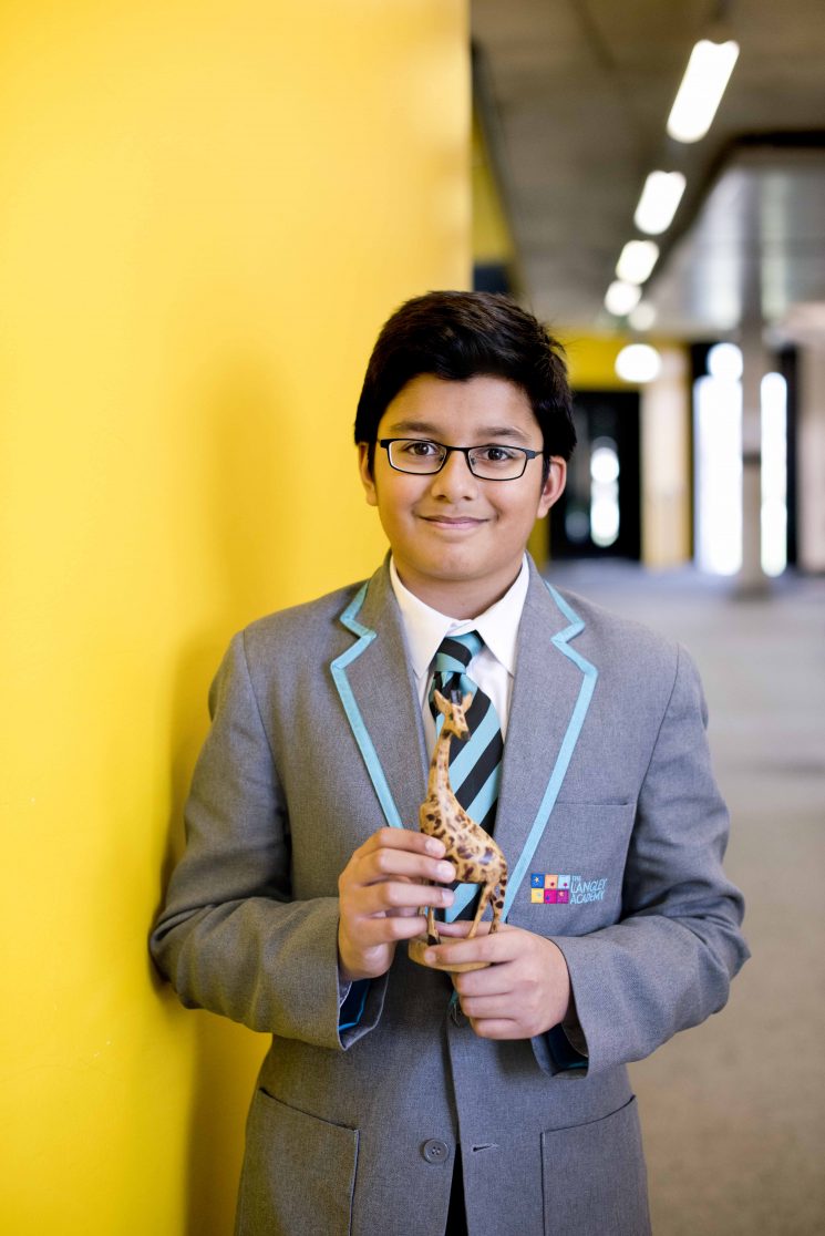 Pupil in uniform holds wooden giraffe in corridor of school.