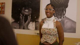 Zhara Elizabeth with her artwork Hidden in our Hair, displayed in the community gallery space at the Migration Museum in Lewisham, London. Photography by Felix Ursell.